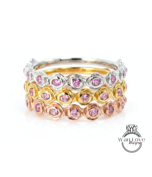 A stack of rings with pink gemstones in various colors, including silver, gold, and rose gold.