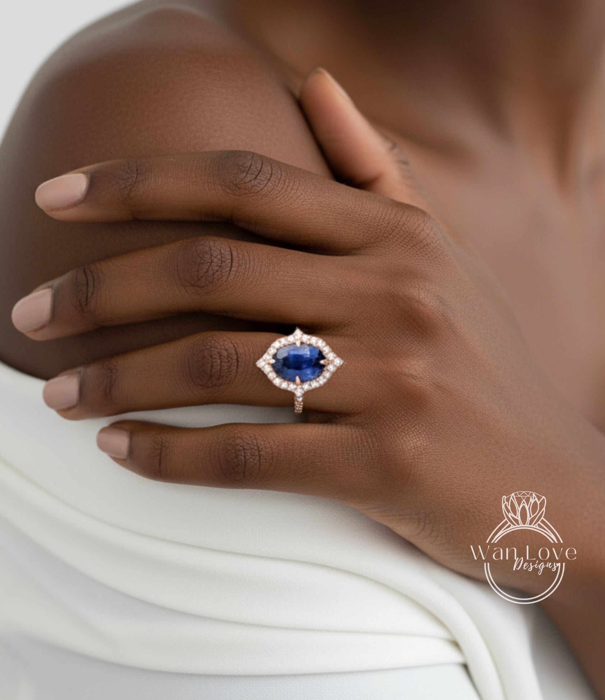 A close-up of a person's hand wearing a ring with a large blue gemstone, resting on a white fabric.