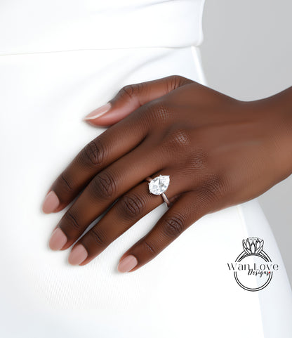 A close-up of a hand wearing a diamond engagement ring, with a white dress visible in the background.