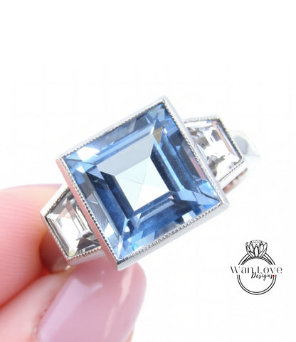 A close-up image of a person's hand holding a ring with a large blue gemstone, likely a diamond.