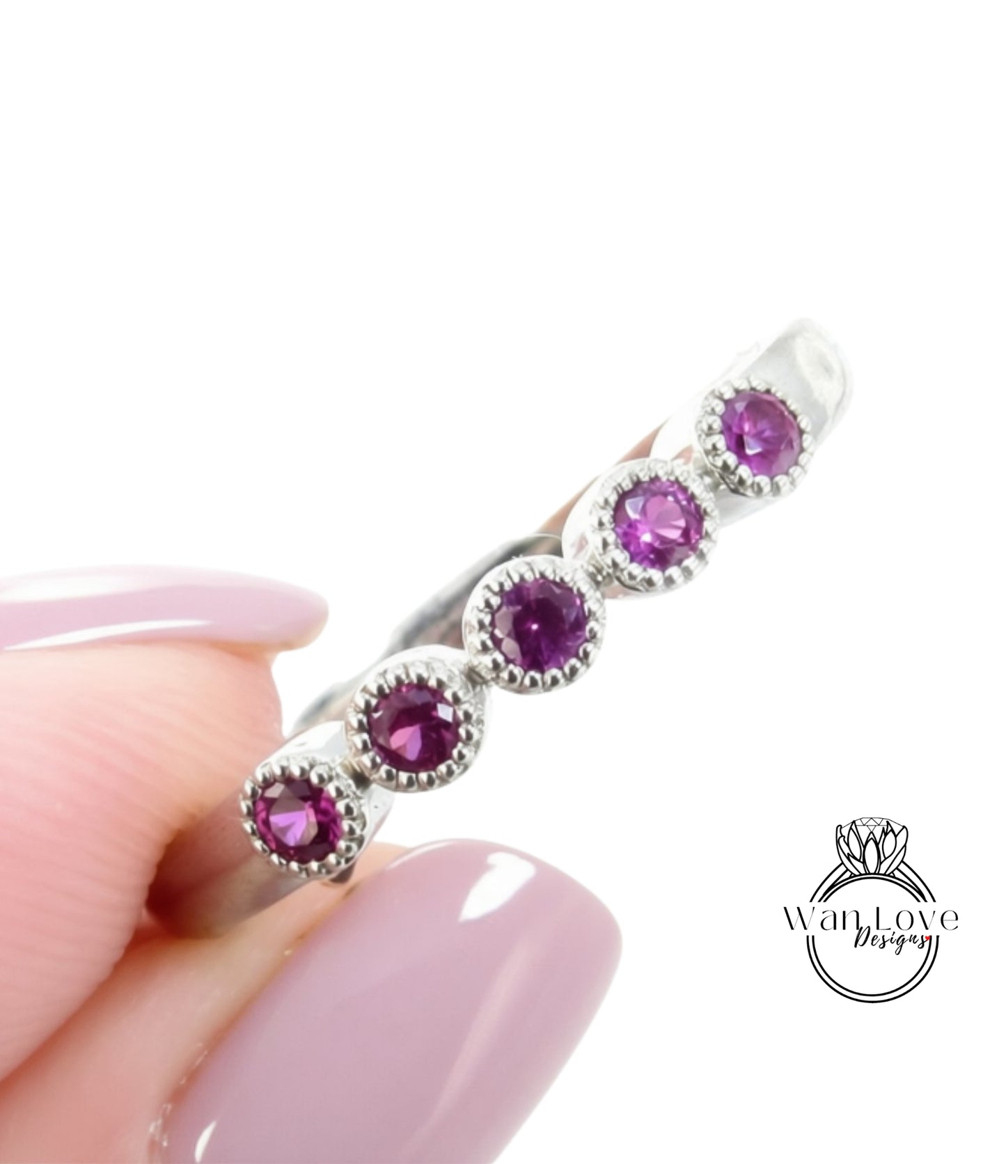 A close-up image of a person's hand holding a silver ring with five purple gemstones.