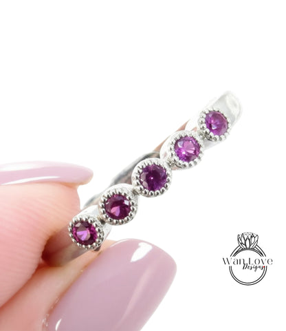 A close-up image of a person's hand holding a silver ring with five purple gemstones.