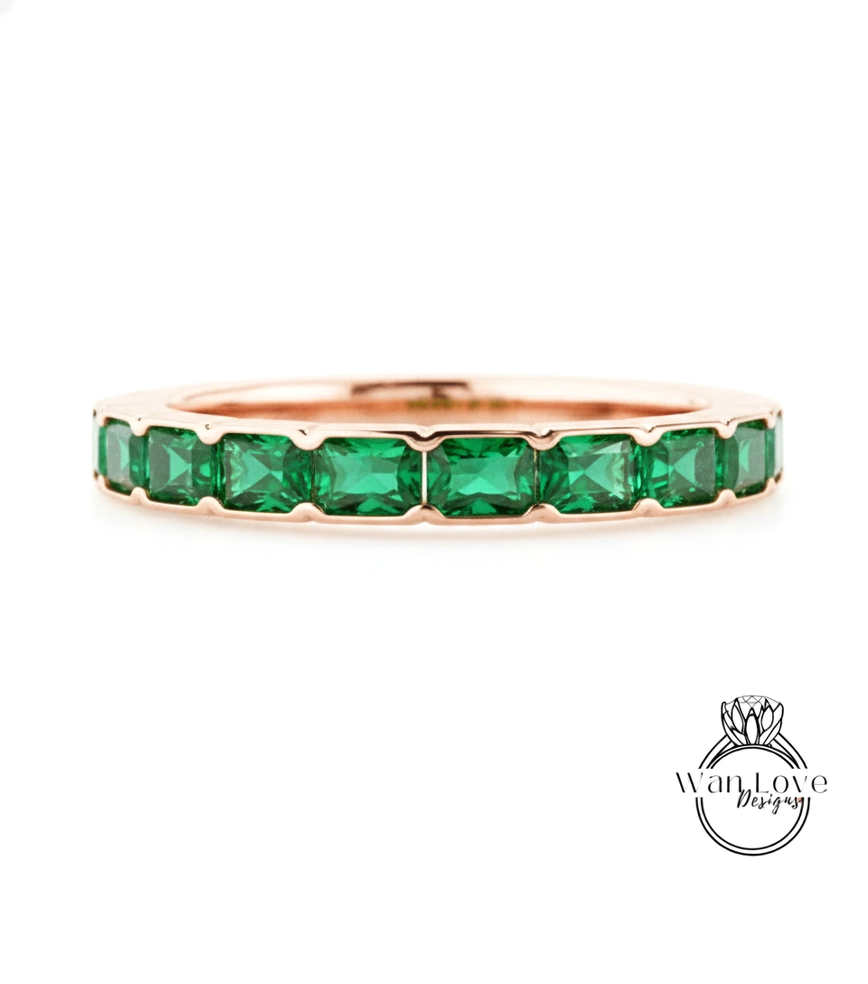 A rose gold band with a row of green gemstones, likely emeralds, set in the center.