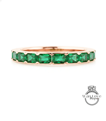 A rose gold band with a row of green gemstones, likely emeralds, set in the center.
