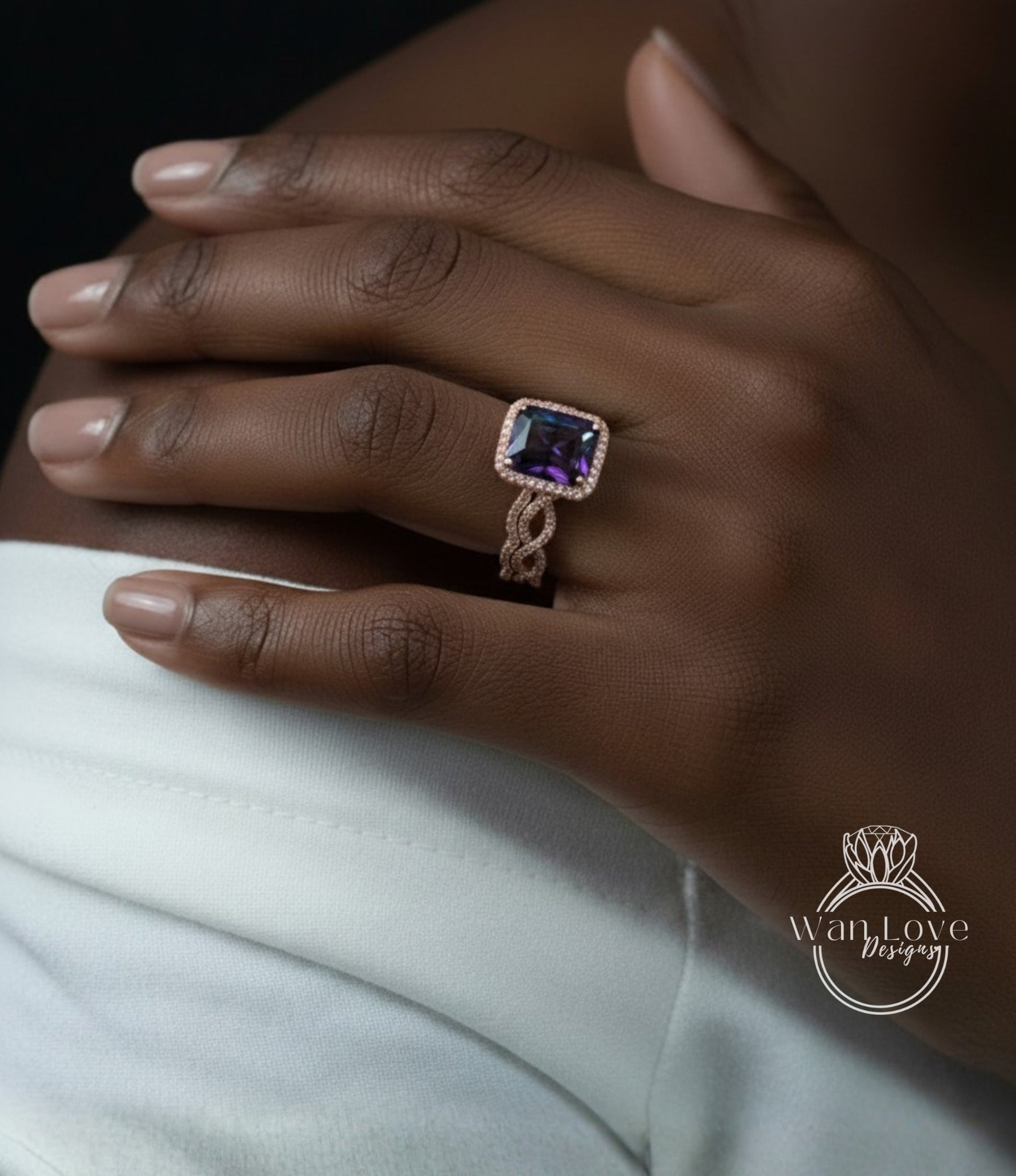 A close-up of a hand wearing a ring with a large purple gemstone, resting on a white fabric.