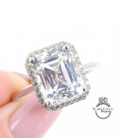 A close-up image of a person's hand holding a diamond ring with a large, clear gemstone set in a halo of smaller diamonds.