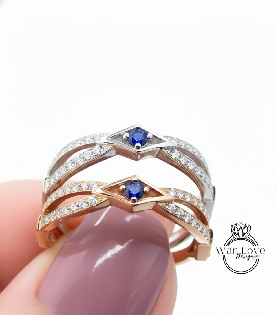 A close-up of a person's hand holding a ring with two gemstone stones, one blue and one silver, against a white background.