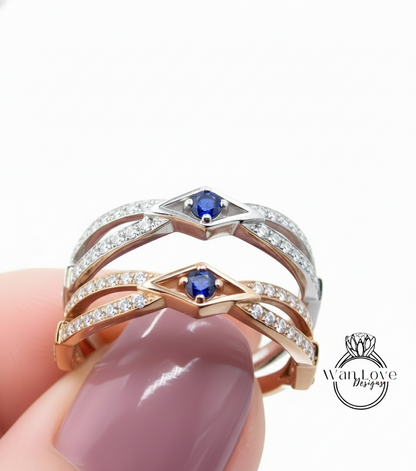 A close-up of a person's hand holding a ring with two gemstone stones, one blue and one silver, against a white background.