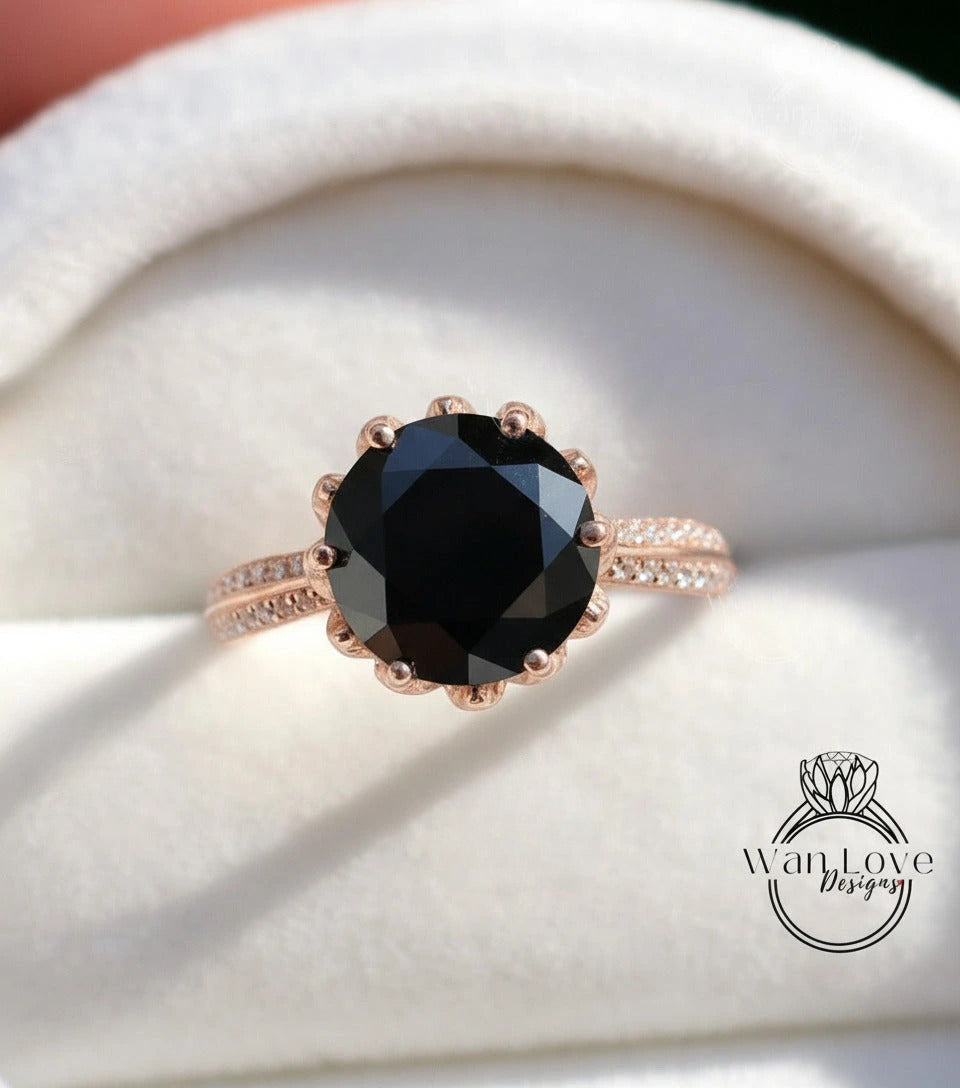 A close-up image of a rose gold ring with a large black diamond as the centerpiece, placed on a white velvet background.
