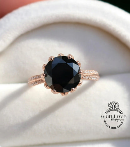 A close-up image of a rose gold ring with a large black diamond as the centerpiece, placed on a white velvet background.