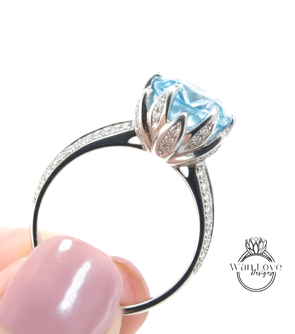 A close-up image of a person's hand holding a silver ring with a large blue gemstone, likely an aquamarine or blue topaz stone.