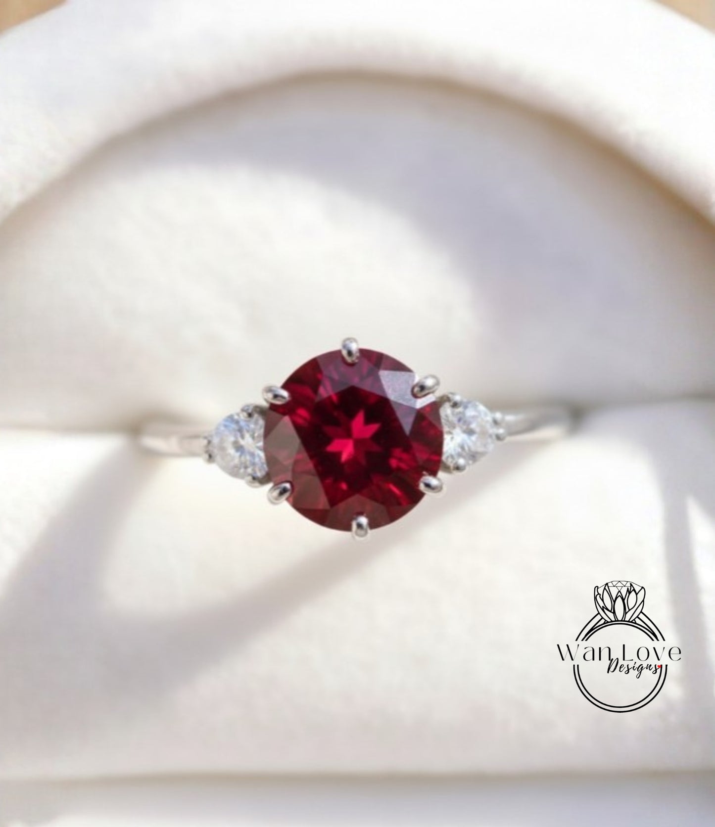 A close-up image of a silver ring with a large, deep red gemstone in the center, surrounded by smaller diamonds.