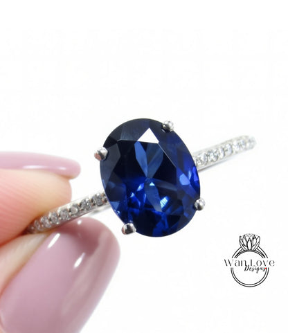A close-up image of a person's hand holding a ring with a large blue gemstone, likely a sapphire or blue topaz.