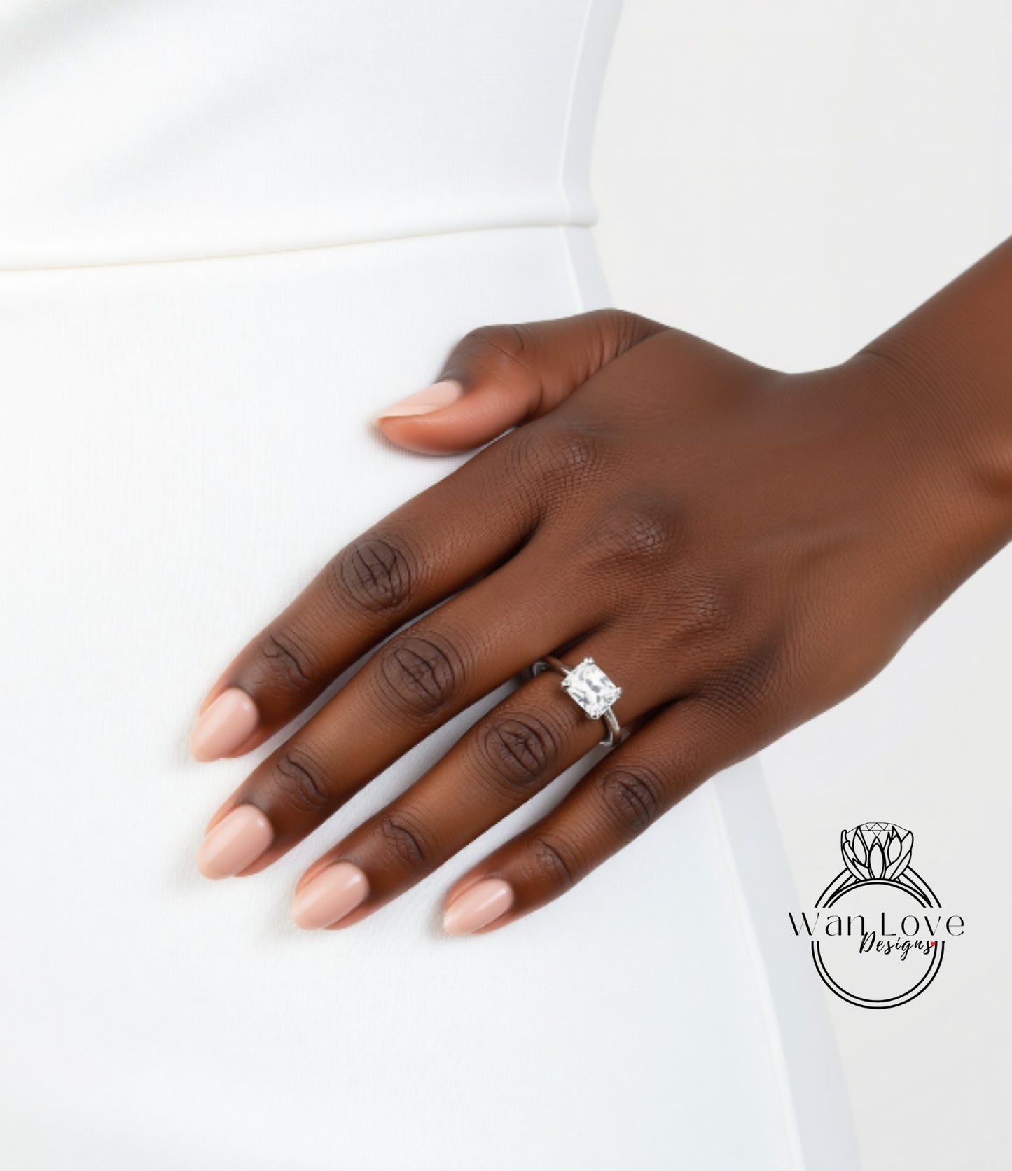 A close-up of a hand wearing a diamond engagement ring, resting on a white surface.